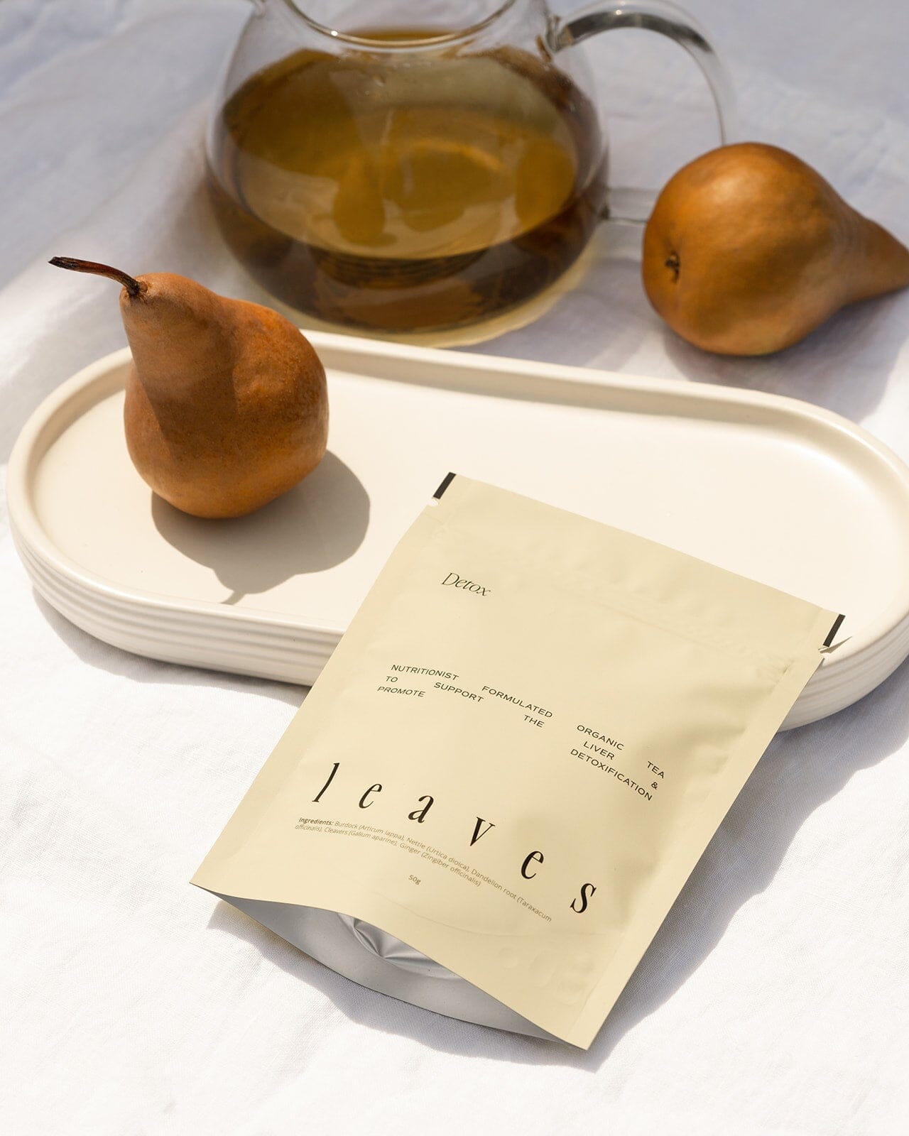 Detox tea pouch laying down next to a pear