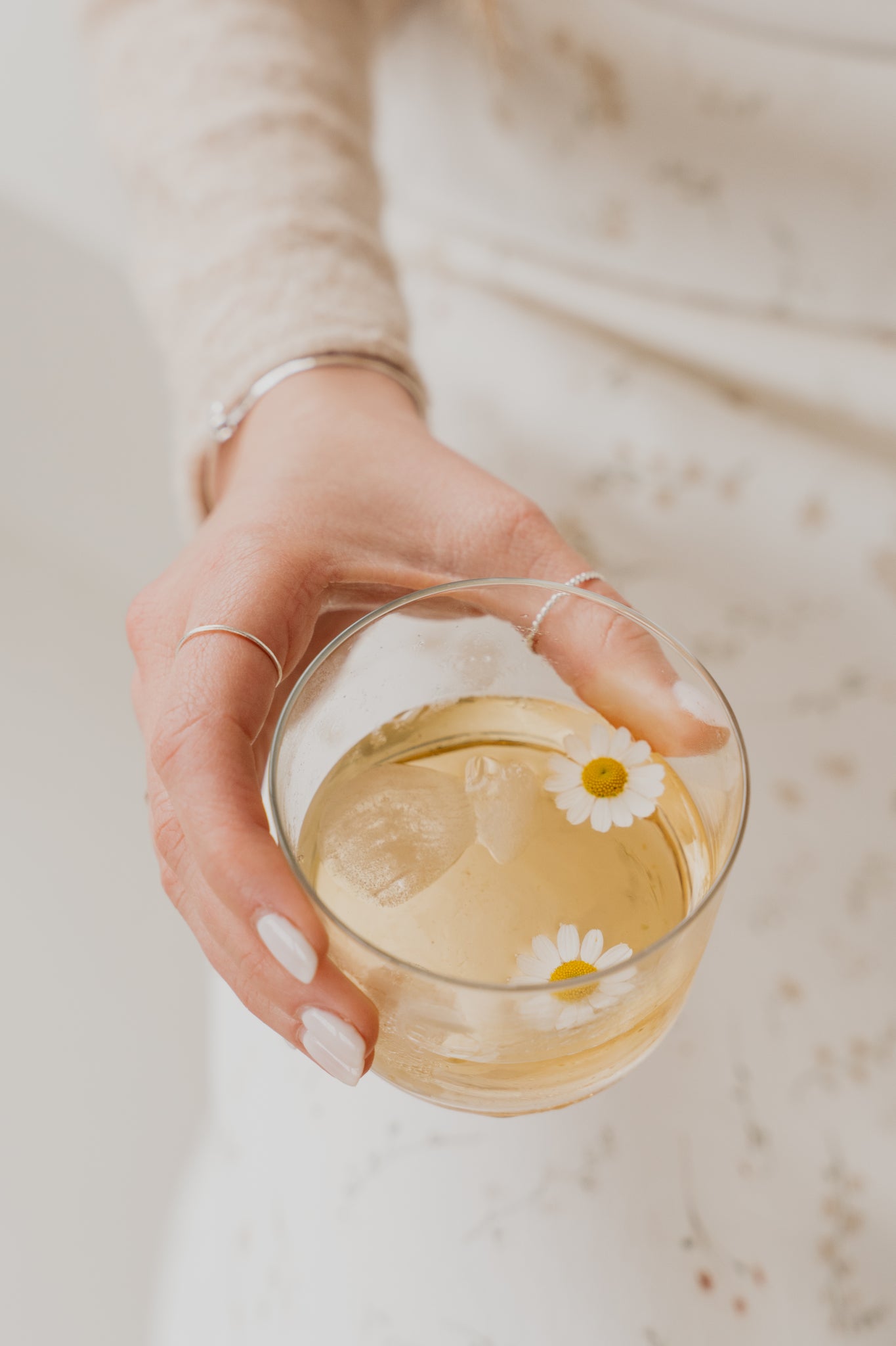 Woman's hand holding a clear glass with tea with daisies in it