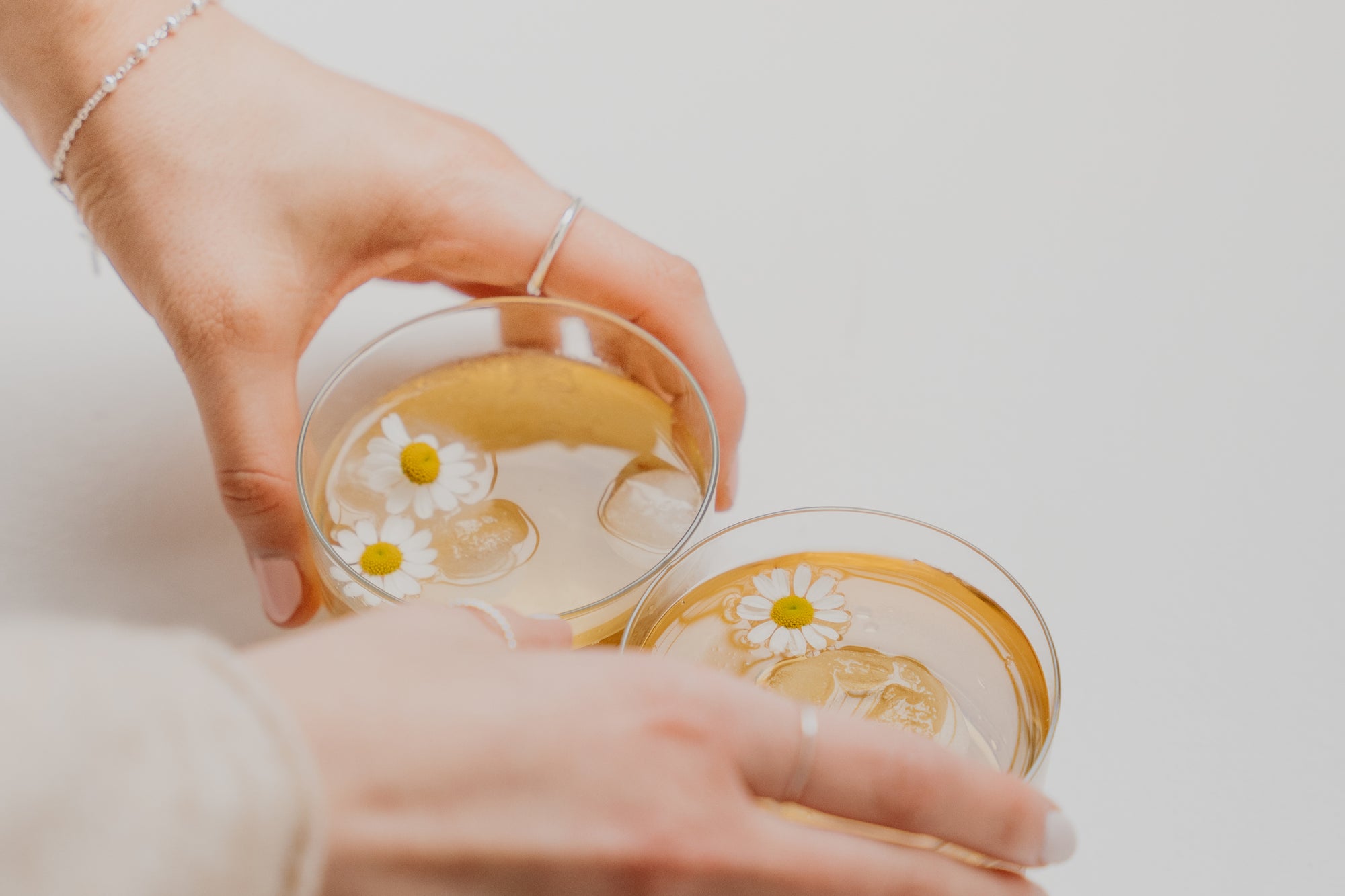 Woman's hands holding two cups of tea with daisies in them